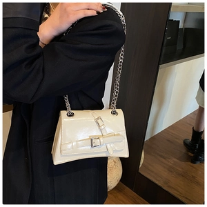 Detail view of beige patent leather shoulder bag with silver chain strap and belt buckle