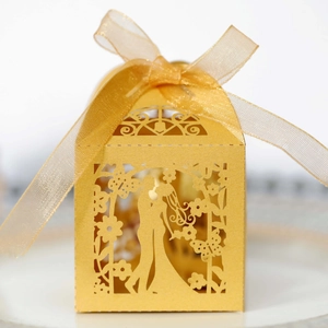 Detail of laser-cut golden wedding favor box with romantic silhouette and ribbon