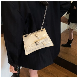 Detail of a creamy white patent leather crossbody bag with silver buckles and chain strap