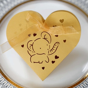 Dettaglio di una scatola di caramelle a forma di cuore con elefante dorato su piatto bianco