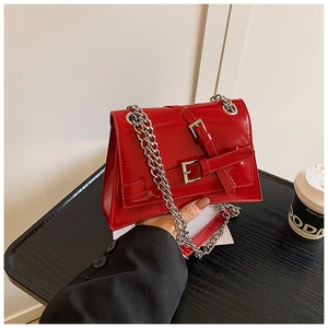 Detail of red patent leather crossbody bag with silver buckles and thick metal chain