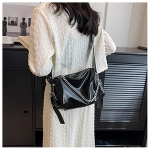 Detail view of a black glossy crossbody bag with silver chain and wide adjustable strap