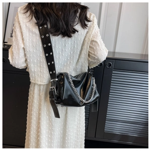 Detail of black glossy shoulder bag with metallic eyelets and silver chain strap