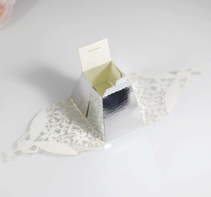 Detail of silver mirror laser-cut favor box with intricate white floral pattern