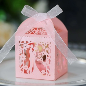 Close-up of pink laser-cut wedding favor box with ribbon detail on a white ceramic plate