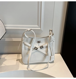 Close-up of minimalist cream bucket bag with crisscross leather straps and silver twist lock