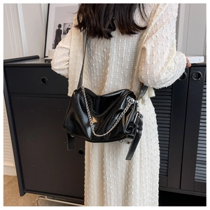 Detail of glossy black PU leather crossbody bag with striking silver metal chain strap