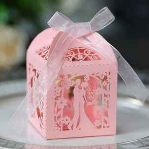 Detail of pink laser-cut wedding favor box with bride and groom silhouette and ribbon