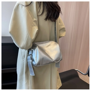 Rear view of silver metallic pillow bag with wide eyelet strap on green coat