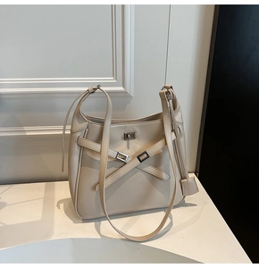 Close-up of beige crossbody bucket bag featuring a metal turn-lock and cross strap detail