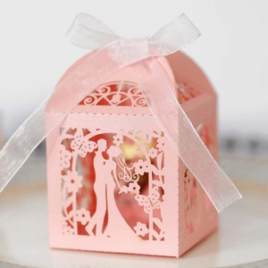 Close-up of laser-cut pink wedding favor box featuring bride and groom with white ribbon bow