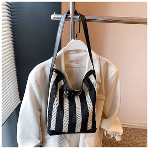 Détail d'un sac cabas en maille rayée noir et blanc suspendu sur un blazer blanc