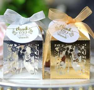 Detail of laser-cut wedding favor boxes with groom and bride silhouette on gold and silver card