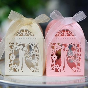 Close-up of laser-cut wedding favor boxes with elegant champagne and pink ribbons