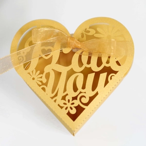 Detail of golden heart-shaped candy box with laser-cut Love You text and silk ribbon