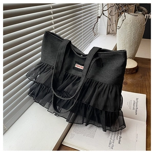 Detail of black denim tote bag with layered mesh ruffles and fashion tag on a windowsill