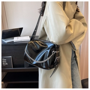 Detail of glossy black leather shoulder bag with silver chain and metal rivets on side