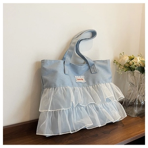 Detailed close-up of light blue denim tote with white lace ruffles and Fashion Bag patch