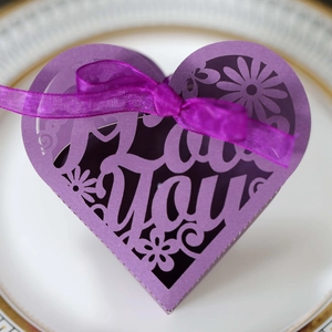 Macro shot of purple heart-shaped gift box with I Love You laser-cut text and ribbon