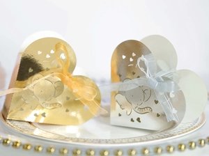 Dettaglio di scatole di caramelle elefante oro e argento con nastri su piatto bianco