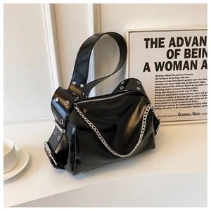 Detail of glossy black patent leather pillow bag with bold silver chain on white podium