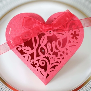 Close-up of red heart laser-cut favor box with Love script and satin ribbon decoration