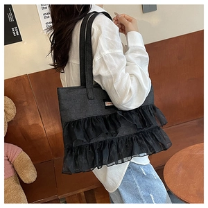 Close-up of black denim tote bag with tiered lace trim worn by a model in a cozy setting