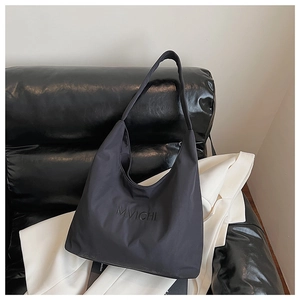 Detail of minimalist black hobo bag on leather sofa with white blazer background