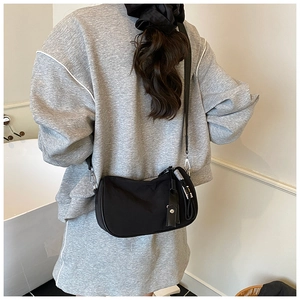 Minimalist black nylon crescent crossbody bag worn by a model in a modern home setting