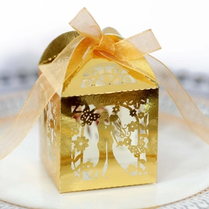Laser-cut wedding candy box with gold silhouette and organza ribbon on ceramic plate