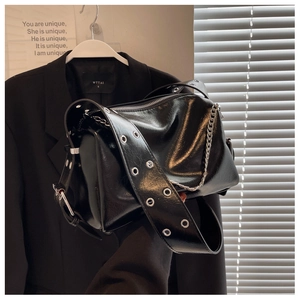 Detail of glossy black pillow bag with wide eyelet strap and silver chain accent