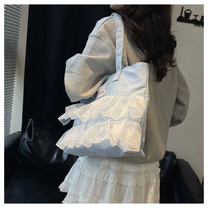 Detail of light blue denim tote with white organza ruffles and fashion label on the front