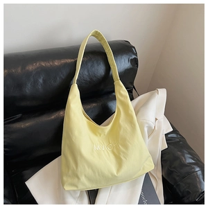 Detail of yellow nylon tote bag with white MVICHI embroidery on a black sofa