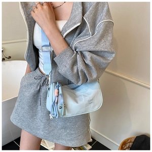 Detail view of light blue crossbody bag with a wide strap and decorative tassel