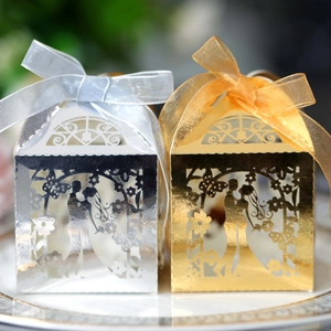 Detail of laser-cut hollow wedding candy boxes in gold and silver with elegant ribbon bows