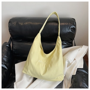 Detail of yellow canvas tote bag with MVICHL embroidery on a stylish black leather chair