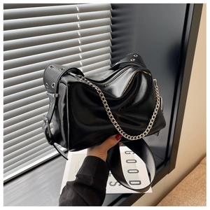 Close-up of black glossy pillow bag with silver chain and metal eyelet shoulder strap