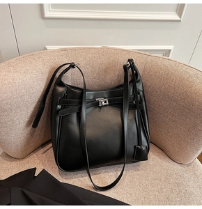 Detail of a black matte leather bucket bag with silver buckle on a beige sofa
