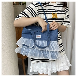 Detail of dark blue denim handbag with white layered tulle lace trim and logo patch