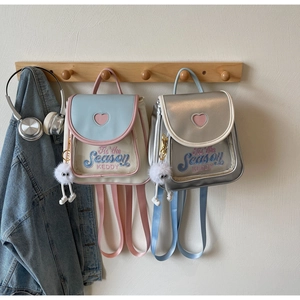 Mini backpacks with heart cutout details and plush charms hanging on a wooden wall rack