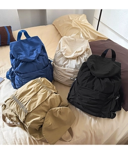 Sacs à dos légers à cordon en bleu, beige, kaki et noir sur un lit douillet