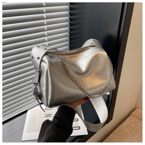 Silver metallic pillow bag with wide eyelet strap and chain detail held by a model
