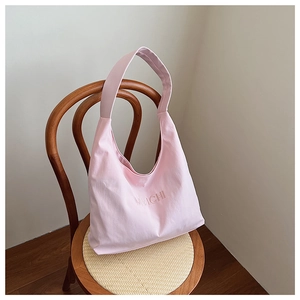 Detail view of pink fabric tote bag with MMICHI embroidery hanging on a wooden chair