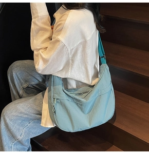 Gros plan d'un sac demi-lune en nylon bleu Morandi avec bandoulière sur bois