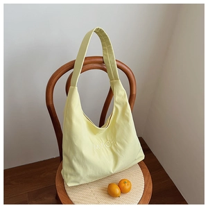 Close-up of yellow canvas hobo bag with MVICHI embroidery hanging on a dark wood chair