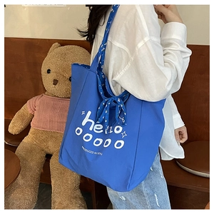 Detail of blue canvas tote bag featuring white printed text and a floral silk scarf handle