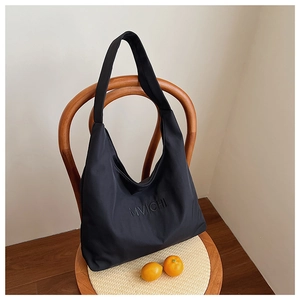 Detail of black Hobo tote bag with embossed logo on rustic chair with oranges