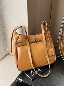 Brown faux leather bucket bag with silver twist lock and side charm beside books