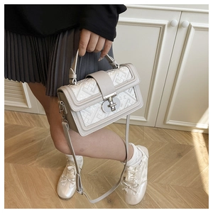 Detail view of the silver metal twist lock on a beige geometric textured small square bag
