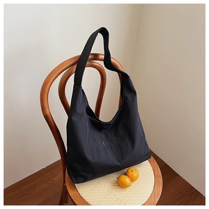 Detail of black nylon tote bag with embossed MVICHI logo hanging on a wooden chair
